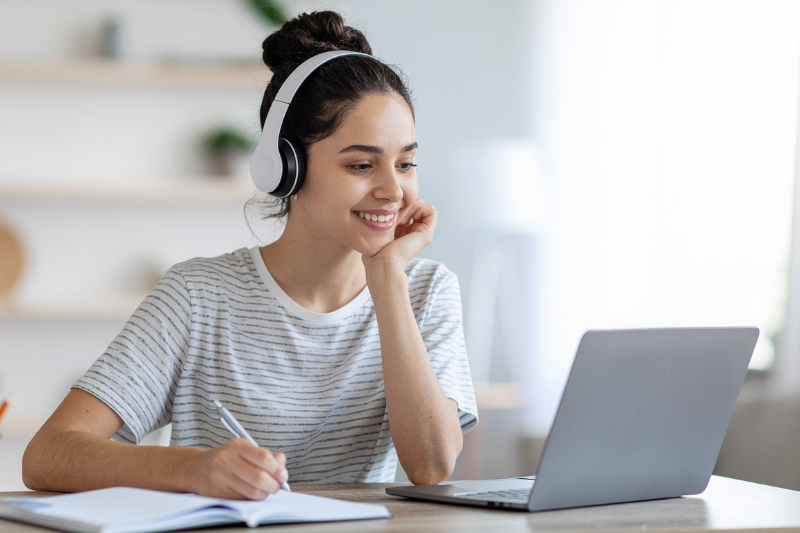 Mulher estudando e trabalhando remotamente em casa com notebook e fones de ouvido, representando o uso de internet residencial para videoconferências, aulas online e envio de arquivos.