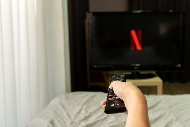 Pessoa assistindo streaming em smart TV em casa com controle remoto, representando o uso de internet residencial para filmes em HD e 4K em plataformas como Netflix, Disney+ e YouTube.